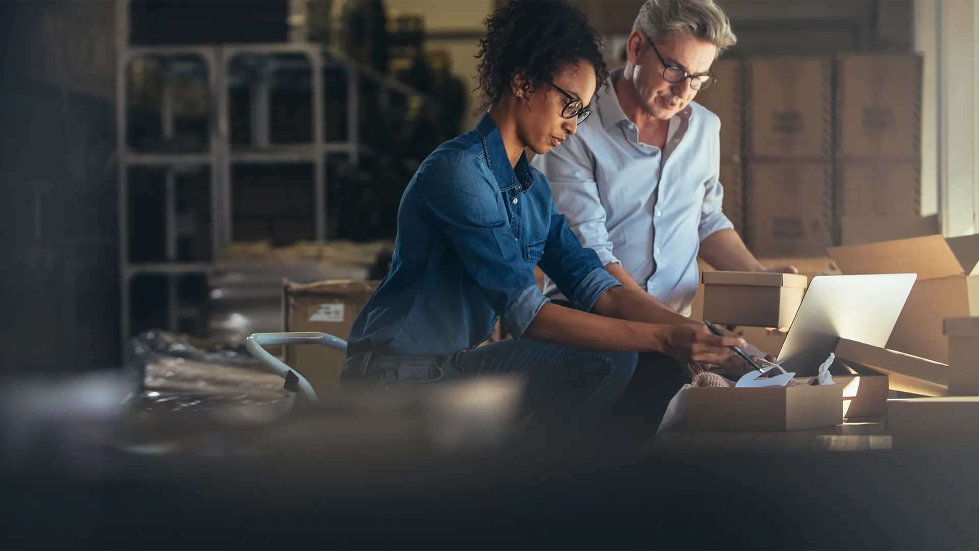 Two people collaborating on a laptop inside a spacious warehouse.