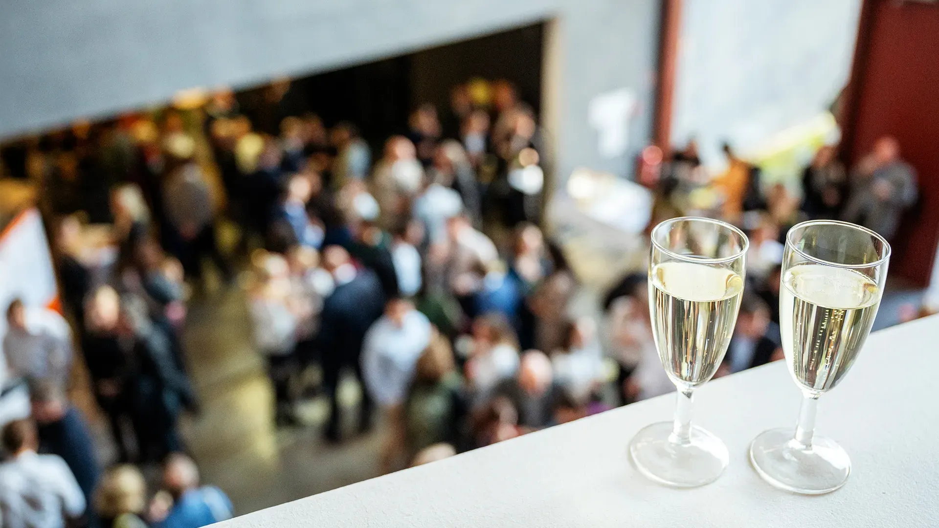 Two glasses of champagne on a table, with a blurred crowd celebrating in the background.