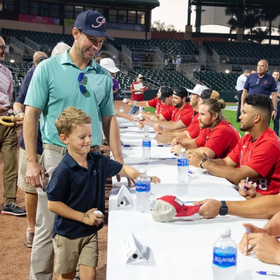 Players signing autographs for excited children at a lively baseball game.