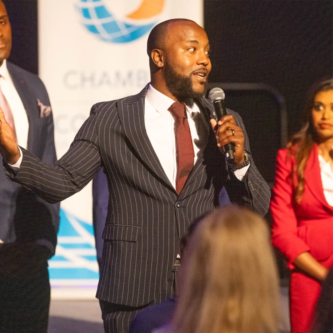 Man in a suit and tie speaks into a microphone during a presentation.