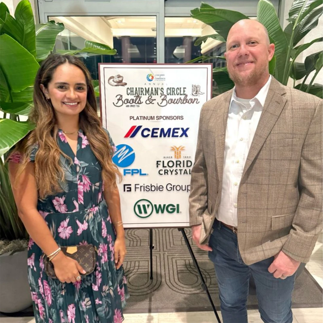 Two people smiling while standing in front of a colorful sign with text and graphics.